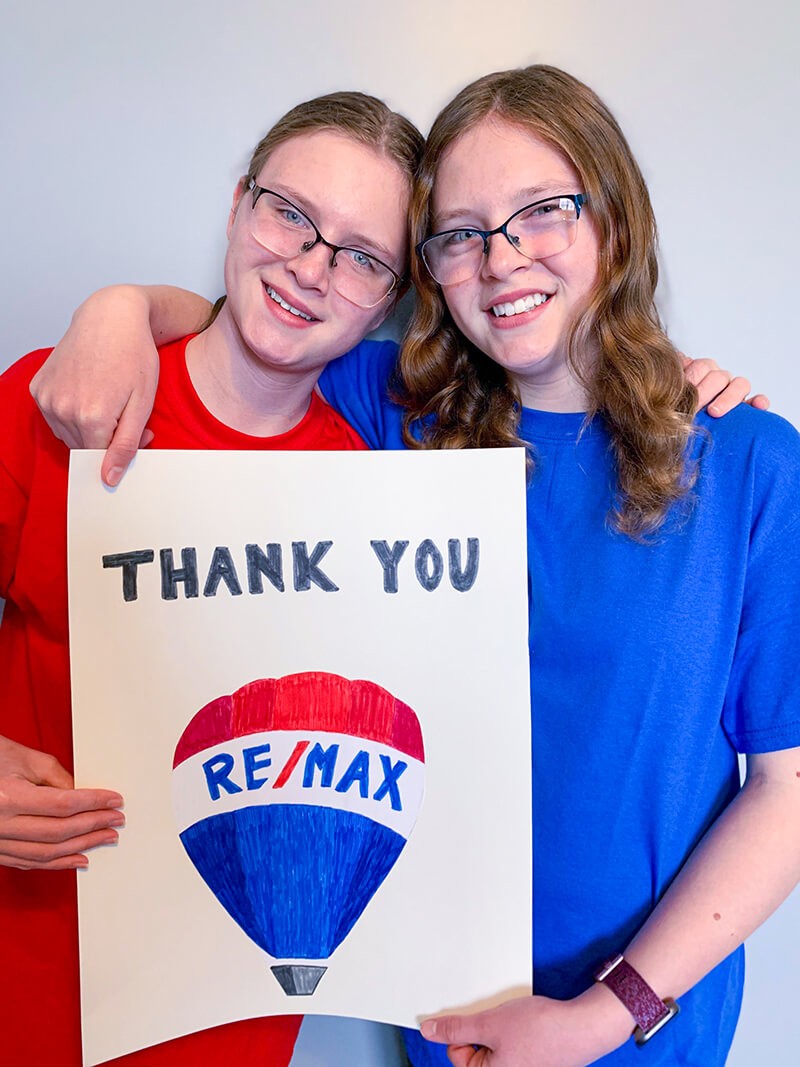 2 girls holding Remax thank you sign